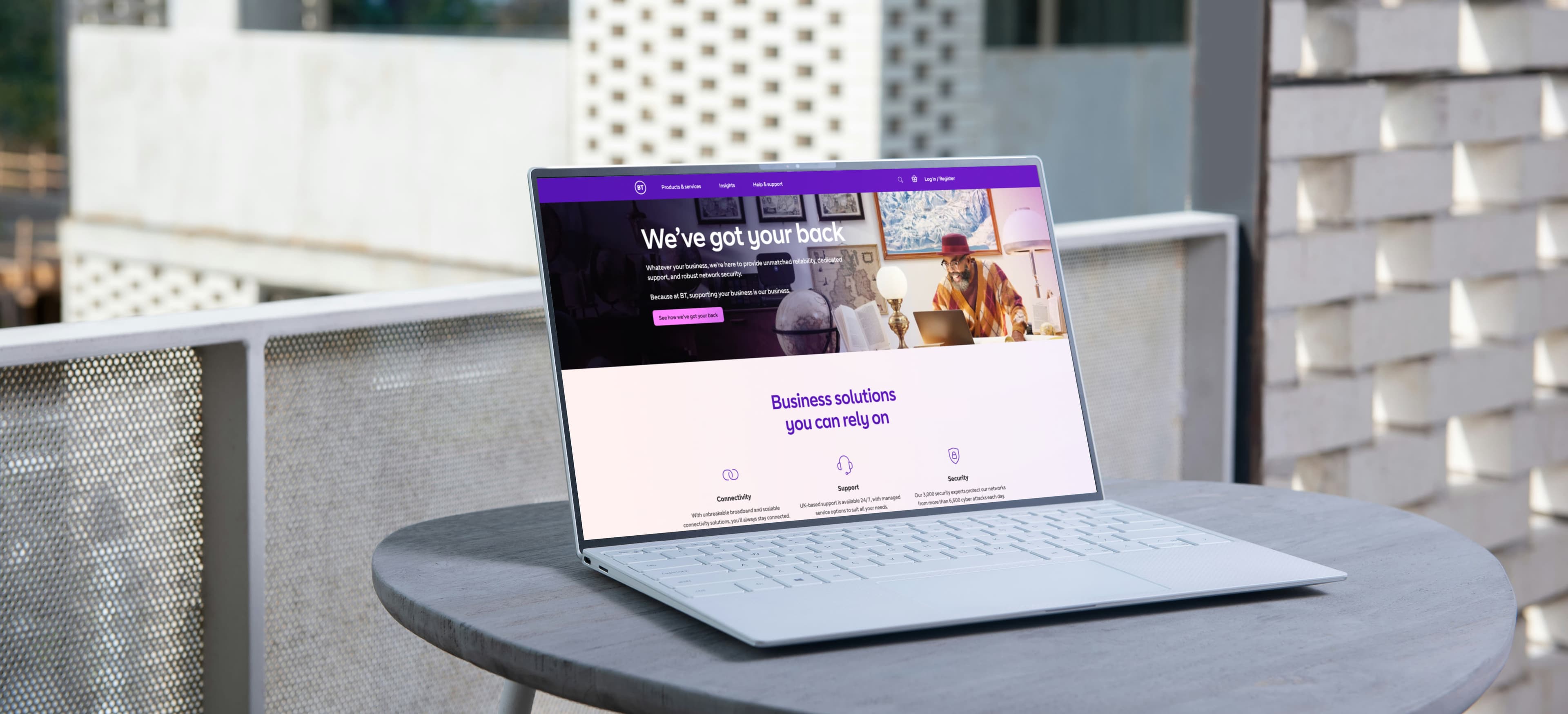 A laptop on a balcony table displays BT's business solutions website, with a headline reading "We've got your back" and sections highlighting connectivity, support, and security.